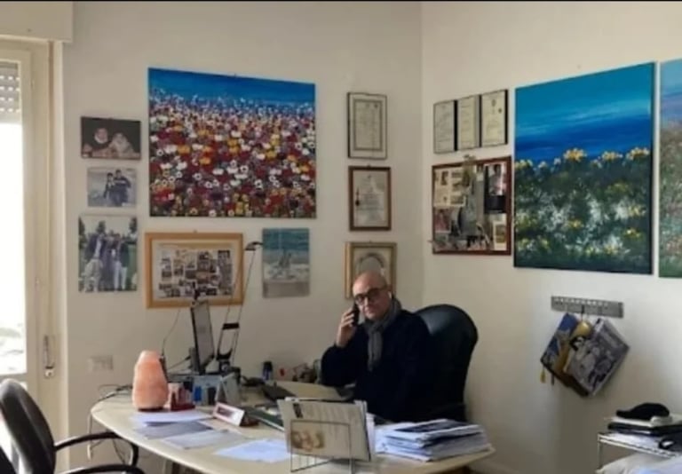 Man wearing glasses sitting at desk in office with photographs and artwork on walls